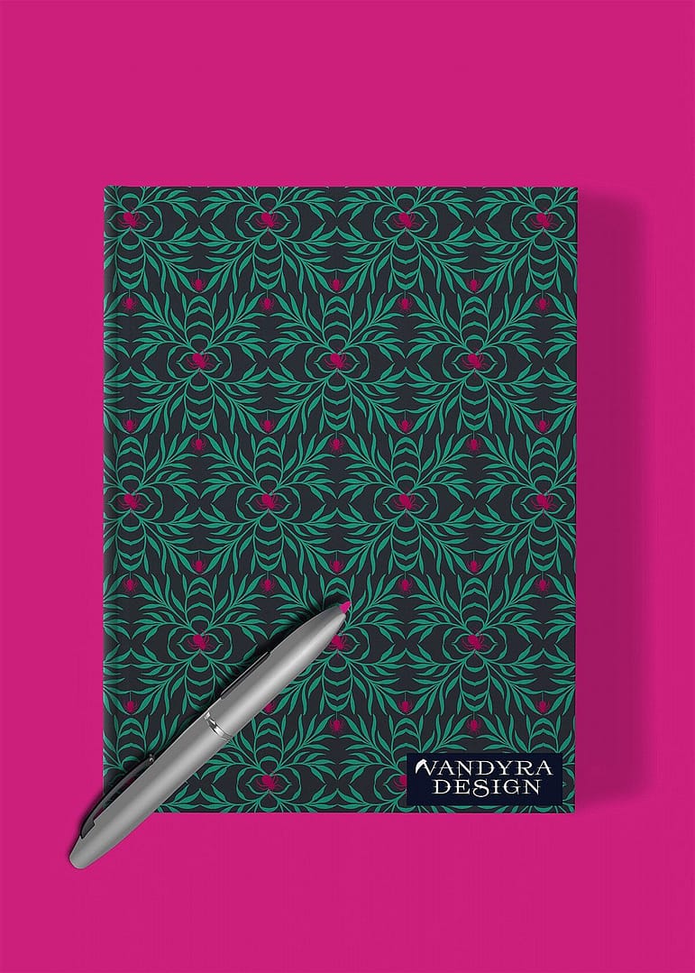 Notizbuch mit Spinnenmuster. Auf dem Notizbuch liegt ein grauer Kugelschreiber. Die Farben des Musters sind Pink, Mint und Schwarz. Der Hintergrund des Bildes ist strahlendes Pink. Auf dem Bild ist das Label - der Schriftzug Vandyra Design von der Designerin zusehen.