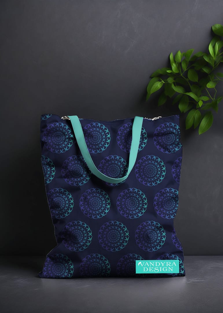 Stoffdesign. Tasche mit Vogelmuster. Motiv eines Vogelschwarm im Kreis. Das Muster ist Mint-Blau-Mitternachtsblau. Auf dem Bild ist das Label - der Schriftzug Vandyra Design von der Designerin zusehen. Der Hintergrund ist dunkelgrau und als Deko sieht man eine Pflanze zum Teil abgebildet.